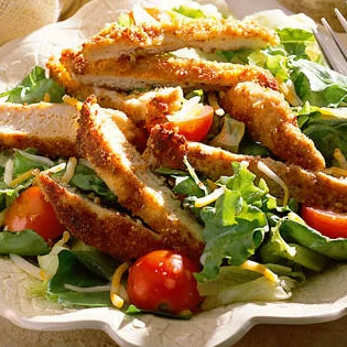 A salad with chicken and tomatoes on top of it.