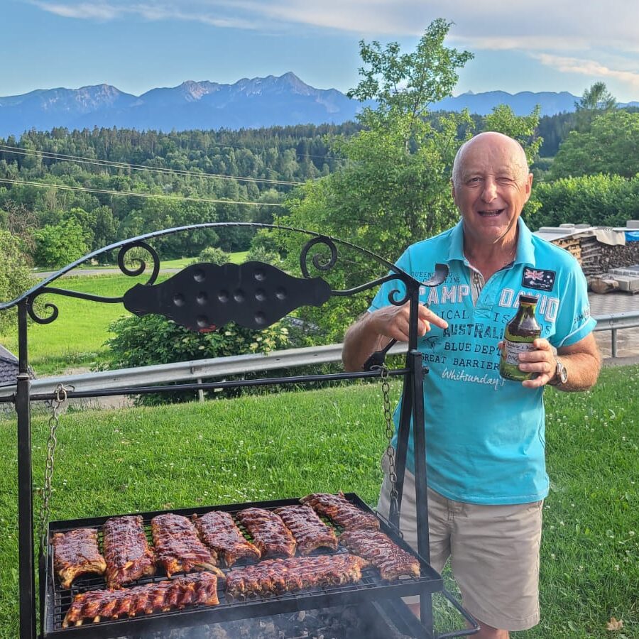 A man standing next to a grill with meat on it.